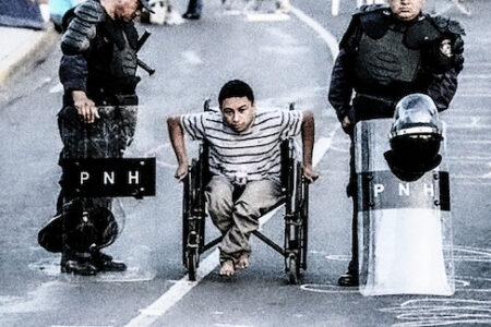 Hondurasilainen ihmisoikeusaktivisti Erlin Mejia kulkee pyörätuolissa kahden mellakkavarusteisen poliisin välistä.