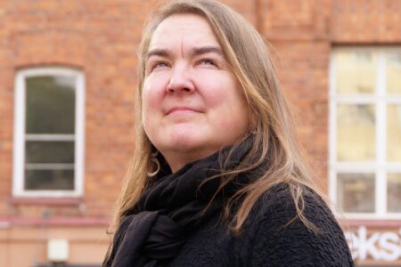 Leena Manninen ulkona taustalla Tekstin talon punatiilinen seinä