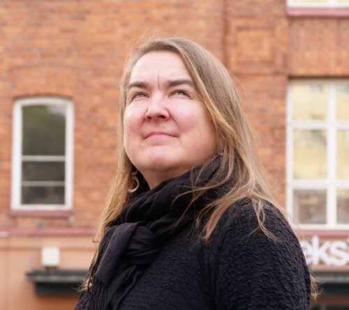 Leena Manninen ulkona taustalla Tekstin talon punatiilinen seinä